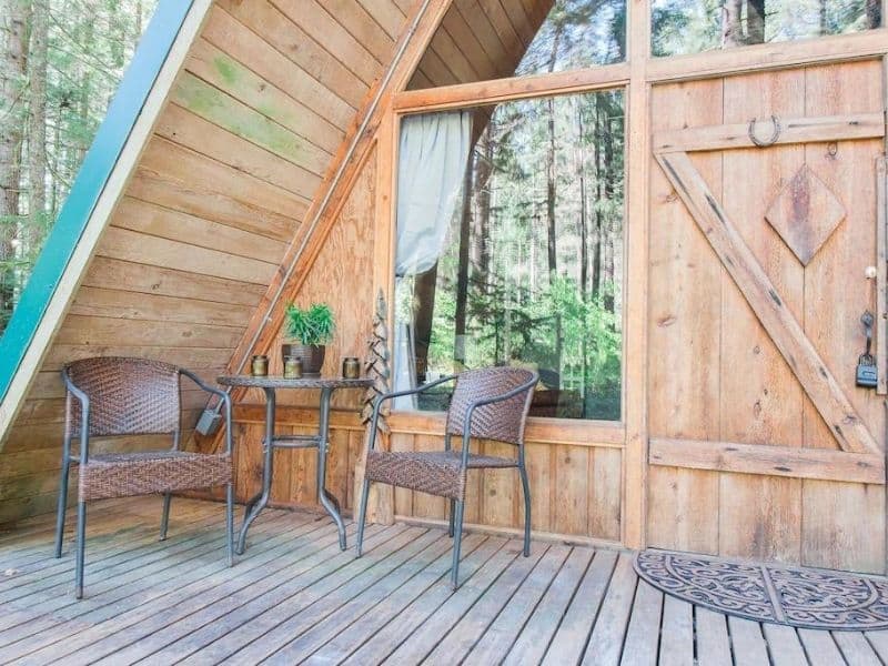 Close-up of exterior entrance to A-frame cabin with wooden door and deck and seating