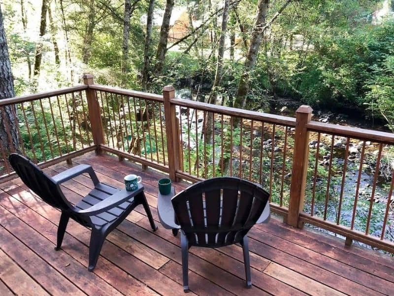 Two chairs on a wooden deck overlooking a river in the woods - part of a guide to the best Mount Rainier cabins to rent