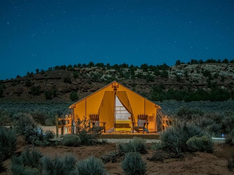 Canvas tent lit up at night with wooden deck and seating at BaseCamp 39, a popular Zion glamping spot