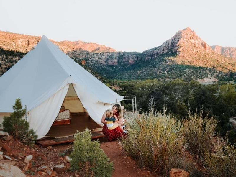 Large canvas glamping tent near Zion National Park with woman sitting outside holding a toddler on her lap