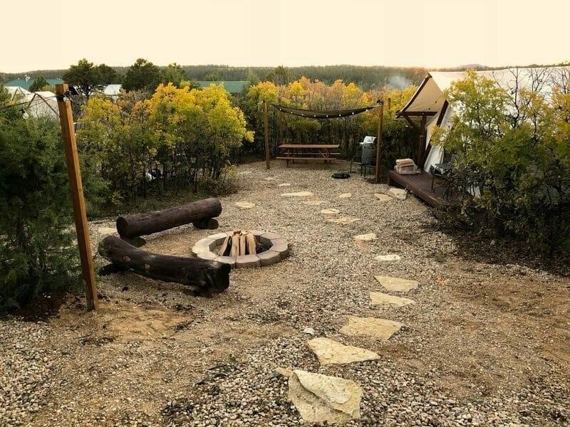Outside view of glamping site at Zion Ponderosa Ranch near Zion NP with fire pit, log seating, and path leading to glamping tent and picnic table