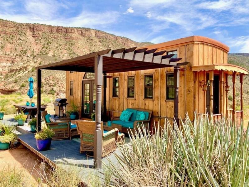 Tiny house at Zions Tiny Oasis with wooden exterior, covered patio, and colorful turquoise seating 