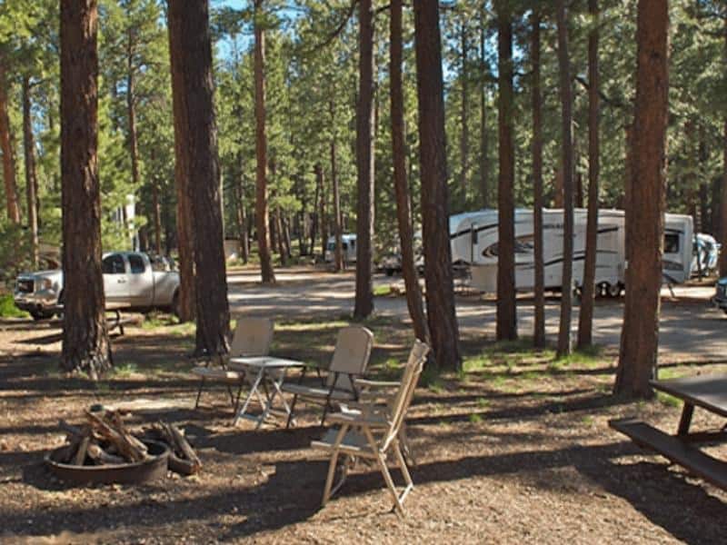 Campsite at Kaibab Camper Village with fire ring, camping chairs and a picnic table with trailers in the background.