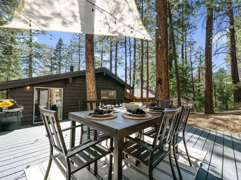 Outdoor dining table on a deck amongst pine trees with a cabin in the background in Big Bear, California.