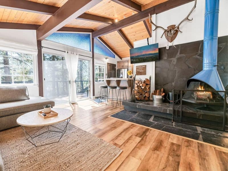 Open plan living and dining area in a luxury Big Bear cabin on Vrbo with vaulted ceilings, a breakfast bar, and a statement blue Swedish fireplace.