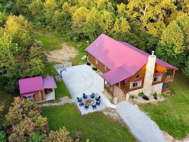 Aerial view of large Hocking Hills cabin with fire pint and basketball court with woodlands surrounding it