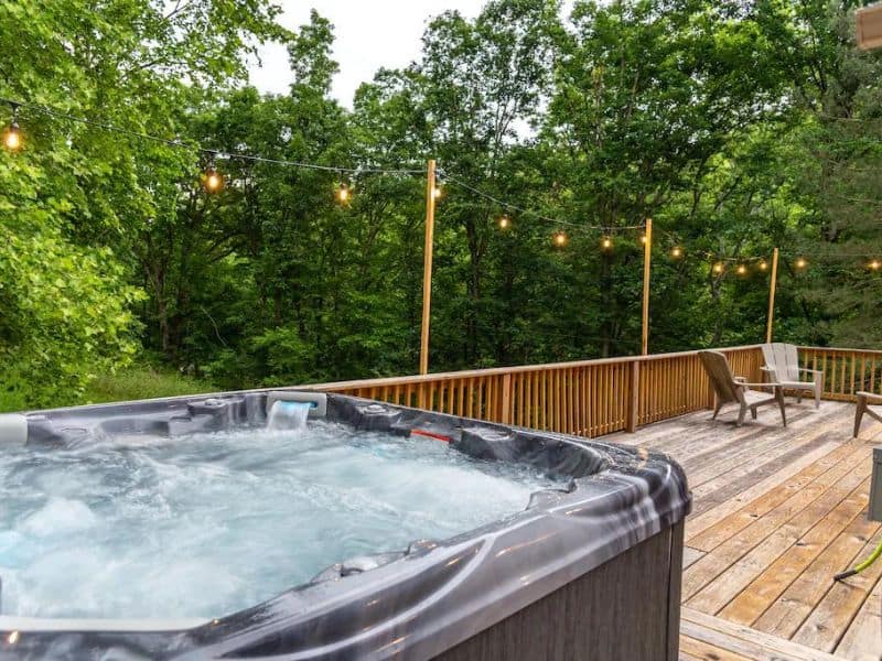Hot tub on wood deck with fairy lights surrounded by woodland