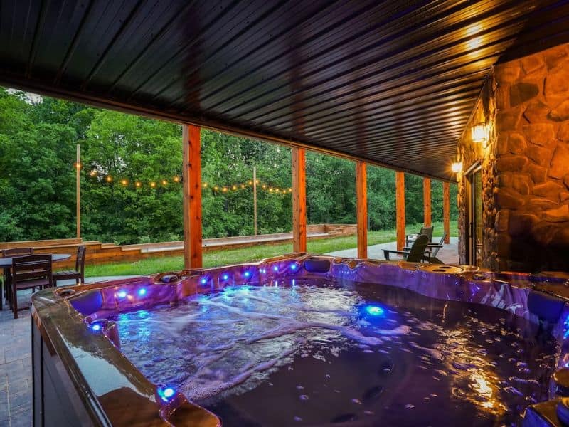 Twilight ambiance in a covered outdoor hot tub area with string lights and forest views at a large cabin in Hocking Hills.