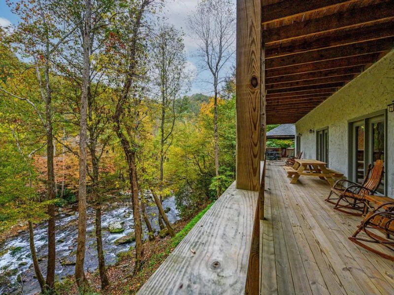 Large wooden deck with rocking chairs overlooking Little Pigeon River at Pigeon Forge Cabin Rental