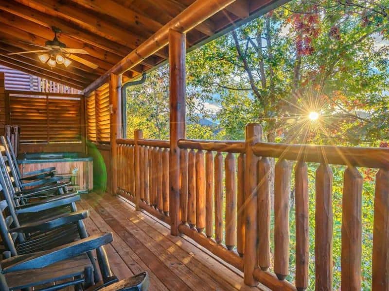 Porch view of Pigeon Forge vacation home, with lounge chairs, and a Jacuzzi tub. Wooden spindle design, looking out into a forest.