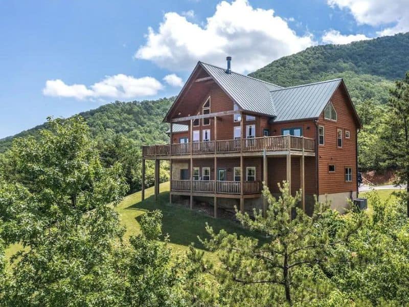 Exterior of Pigeon Forge Cabin with multi leveled porch, located in rolling green hills with trees.