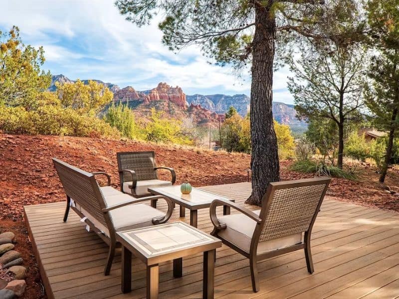 Wooden deck with patio furniture under a large tree with Sedona red rock views in the distance