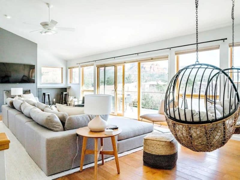 Living room of Sedona rental, with hanging birdcage chairs, extending into a balcony with views of red rock formations.
