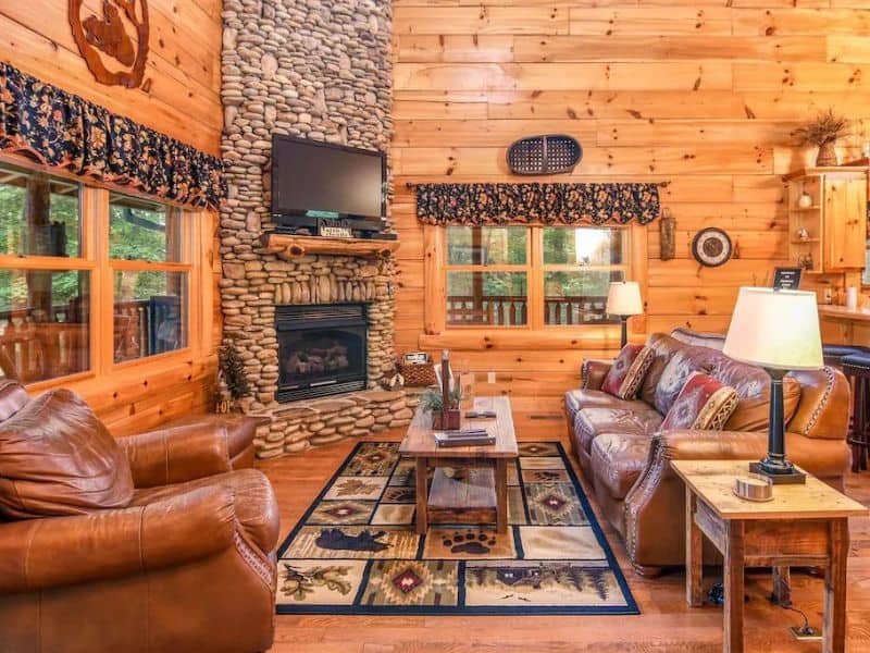 Living area of Pigeon Forge vacation cabin with stone fireplace, floor to ceiling wood paneling, and rustic decor.