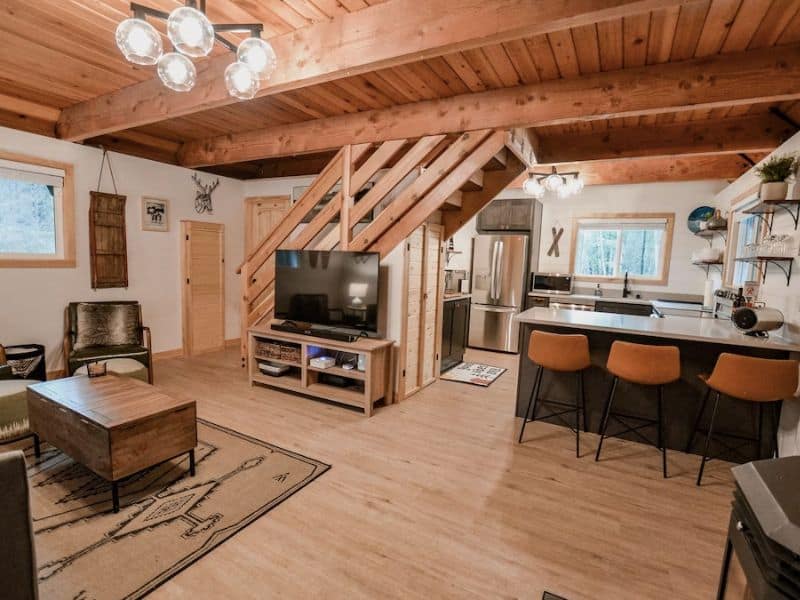 Open living space inside cabin rental near Mount Rainier National Park with small kitchen, barstool seating, large TV, and area rug