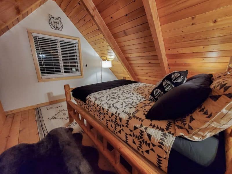 A-frame cabin bedroom with wood ceiling and queen bed facing a window