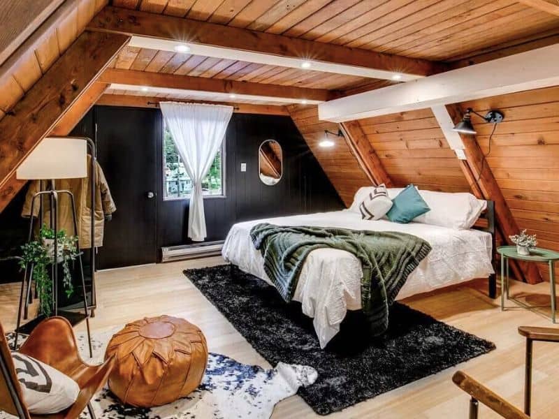 Trendy cabin bedroom with wood ceilings and a large bed with throws and area rugs. Part of a Mt Rainier cabin round-up