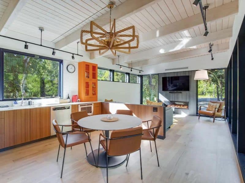 Modern cabin interior of vacation rental near Mt Rainier with circular dining table, funky chandelier, and fireplace with large TV above it