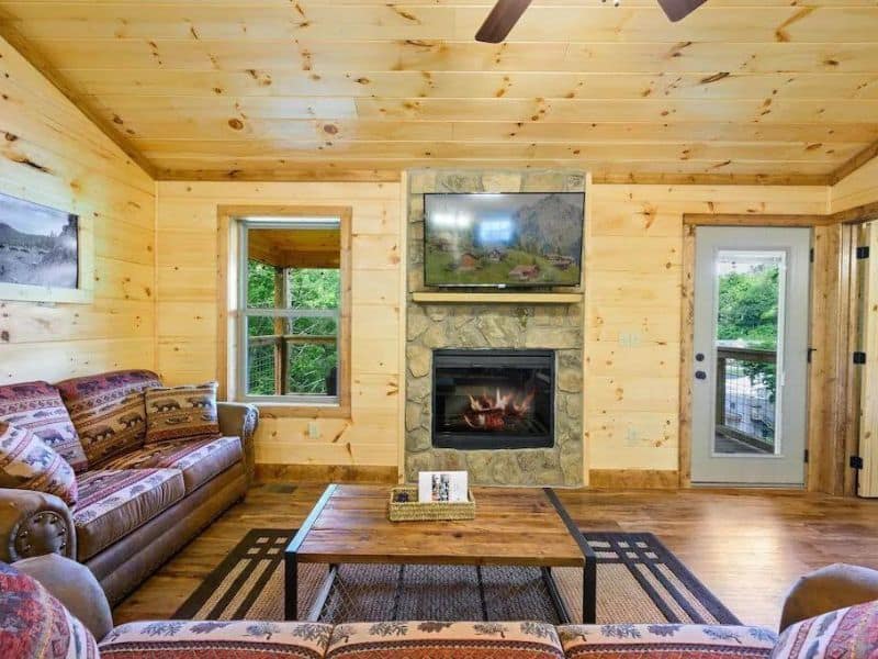Simple living area at Gatlinburg vacation rental with stone fireplace, coffee table, leather couches, and wood finishes