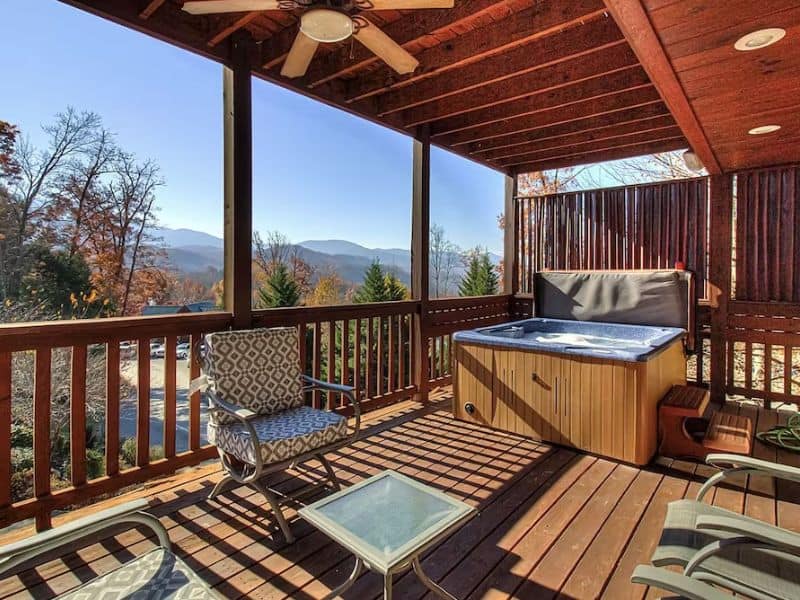 Covered deck with seating hot tub and ceiling fan at Gatlinburg vacation rental