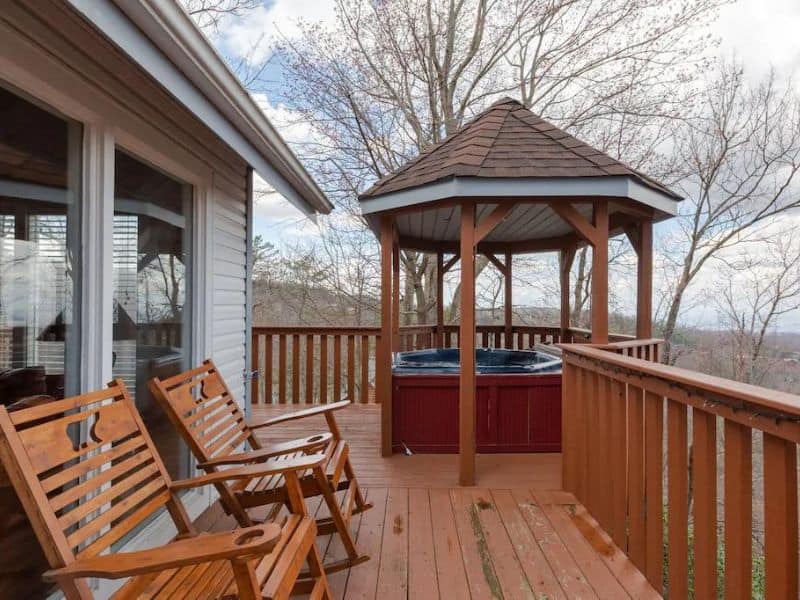 Wooden deck with covered hot tub and rocking chair at pet-friendly Gatlinburg cabin rental