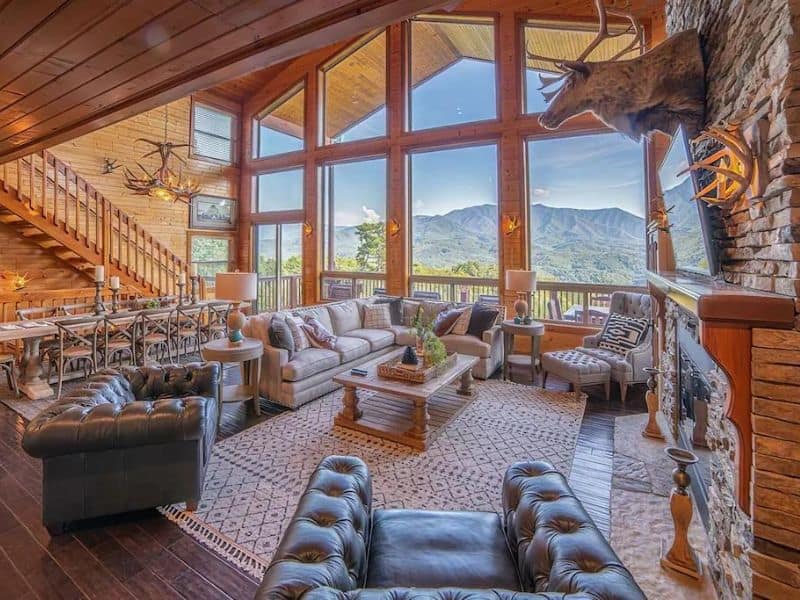 Large open living area in luxury cabin rental in Gatlinburg with floor-to-ceiling windows and lots of plush seating