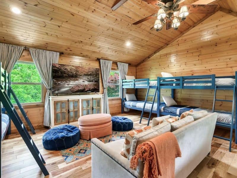 Bunk room with four twin bunks, floor cushions for lounging, and a TV
