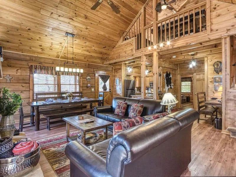 Modern rustic open living space with leather seating, dining area, and kitchen in wood cabin rental in Gatlinburg
