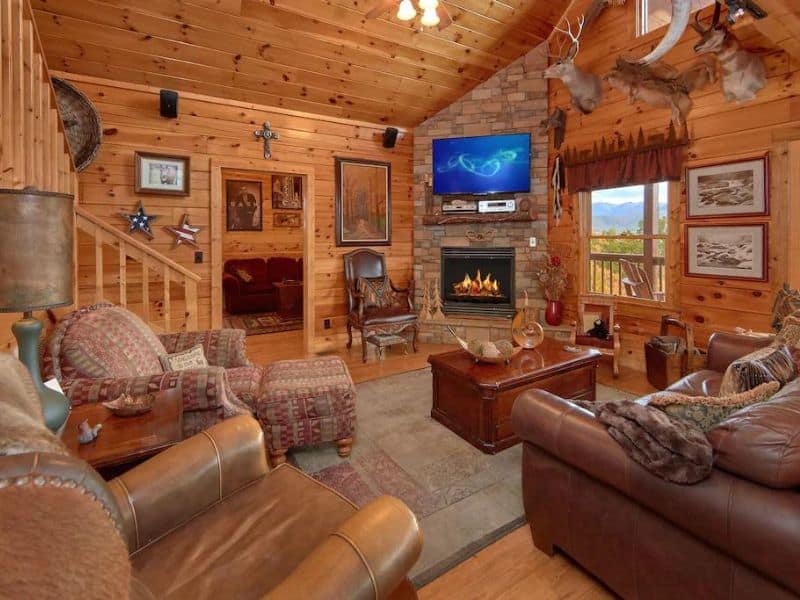 Coy rustic living area in wood cabin rental with stone fireplace and TV