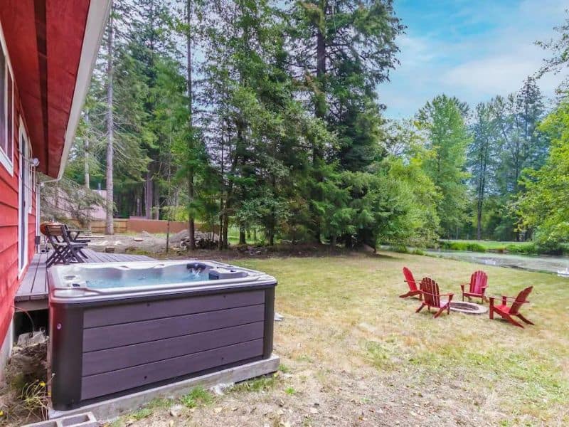 Red cabin with outdoor hot tub and red Adirondack chairs near pond
