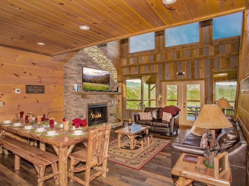 Open plan dining and living area with stone fireplace and large windows at cabin in Gatlinburg