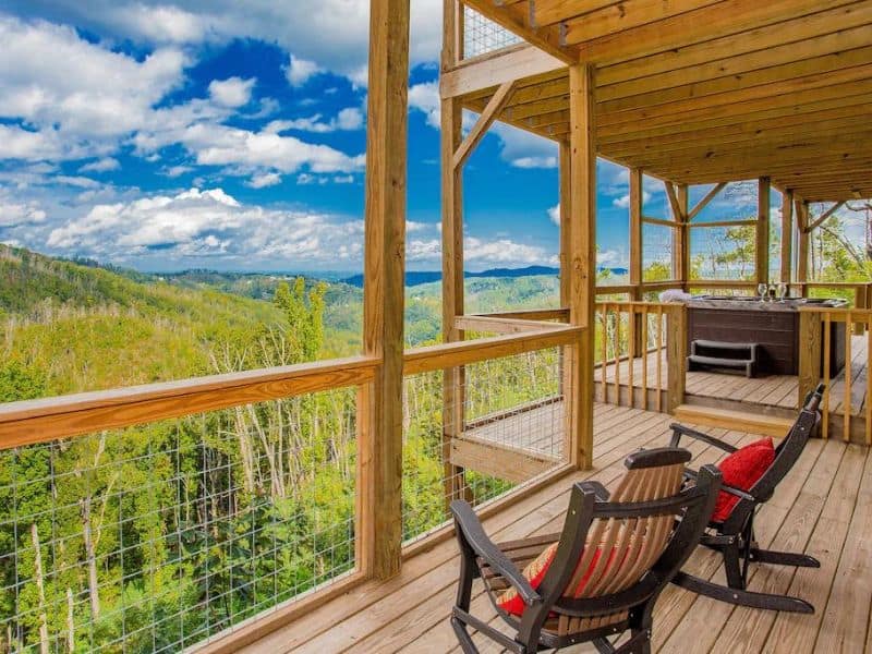 Large deck with rocking chairs and hot tub overlooking the Great Smoky Mountains from a cabin rental in Gatlinburg