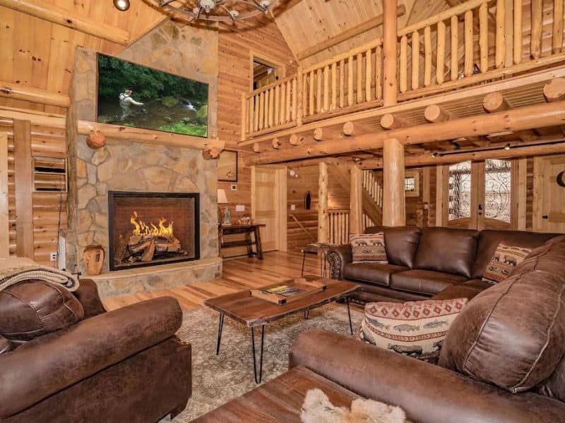 Rustic living area with stone fireplace and leather couches in Gatlinburg cabin rental for large groups