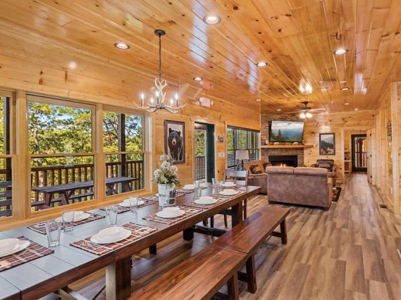 Long dining table with bench seating with comfy living room visible in the background at wood cabin in Gatlinburg