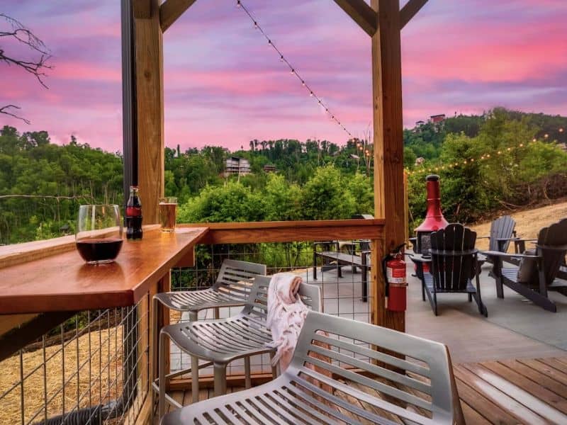 Outdoor entertainment area with fireplace, seating, and bar at a Gatlinburg Vrbo cabin capable of hosting large groups