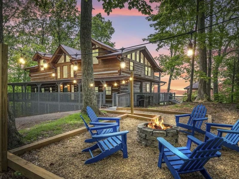 Exterior of large wood cabin rental in Gatlinburg with string lights and blue Adirondack chairs around a fire pit