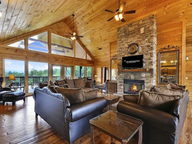 Large open plan living area in Gatlinburg Vrbo cabin rental with stone fireplace, vaulted ceilings and floor-to-ceiling windows