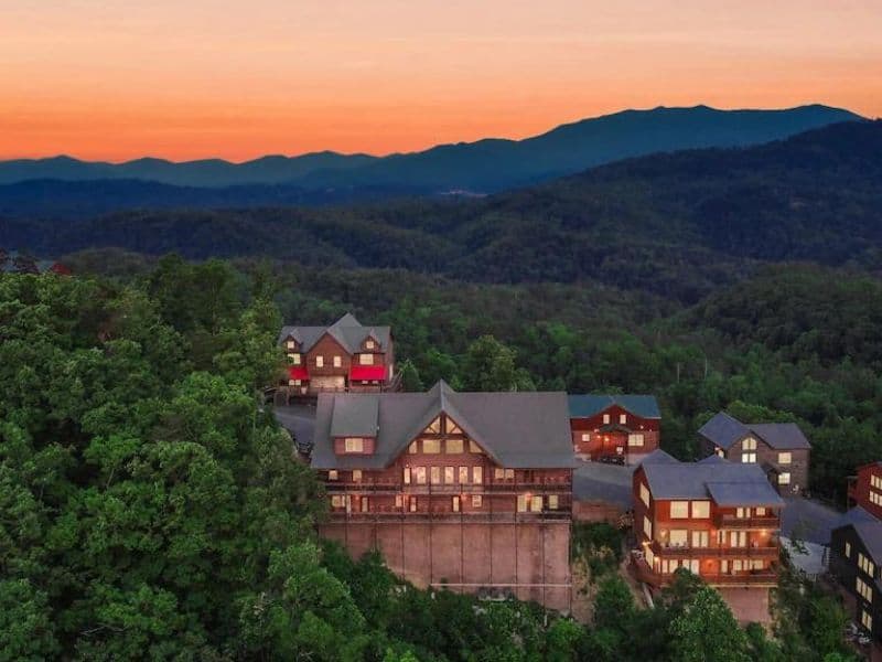 Aerial shot of several large wood cabins in Gatlinburg with a Smoky Mountains sunset in the background