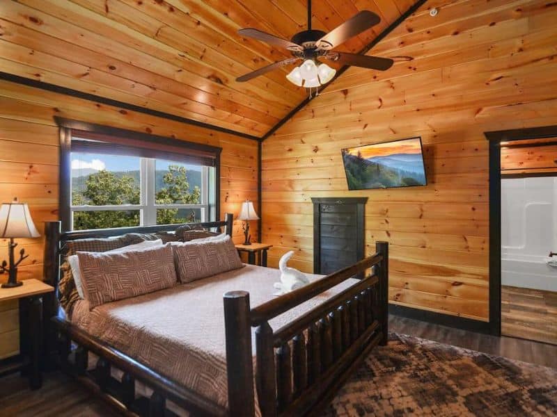 Cabin bedroom with bed, TV, ceiling fan. high ceilings and wood finishes