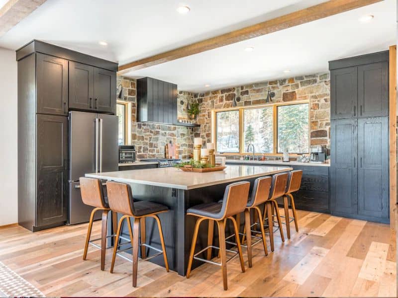 A modern kitchen in a Whitefish MT vrbo with black cabinets, a stone backsplash, and granite counter tops.