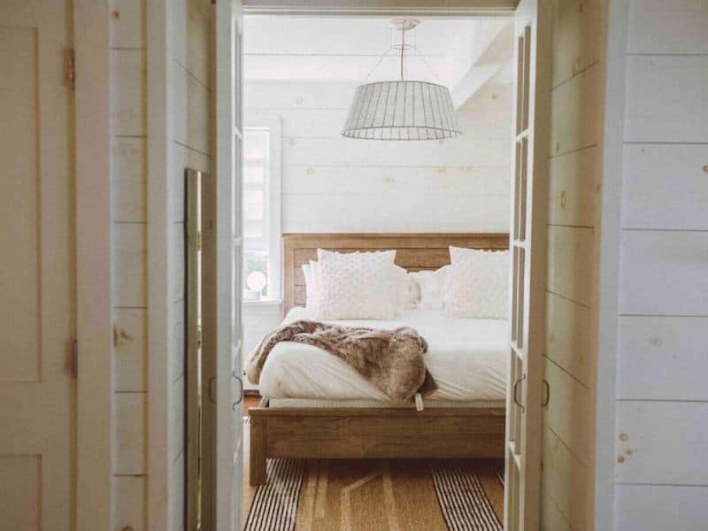Serene bedroom in a Catskills rental with a cozy bed, soft lighting, and a rustic wooden beam ceiling.