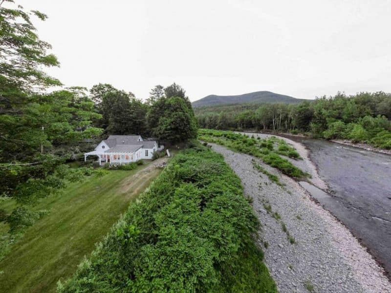Aerial view of a secluded Catskills Vrbo rental property set amidst lush greenery with a river flowing nearby.