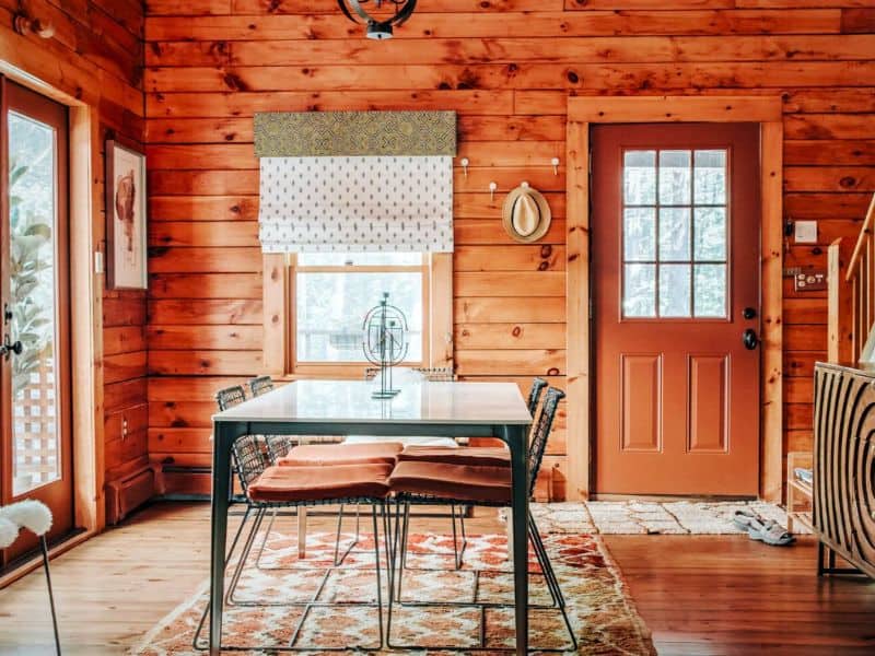 A well-lit dining area in a Catskills rental, showcasing a modern table setting, rustic chairs, and a doorway leading outside.