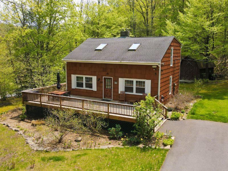 Exterior of a cozy cabin in the Catskills with a wooden deck with outdoor furniture, surrounded by springtime foliage.