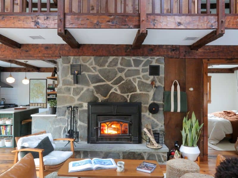 Inviting living area with a stone fireplace in a Catskills Vrbo rental, featuring lofted wooden beams, a cozy seating arrangement, and an open view to the kitchen.