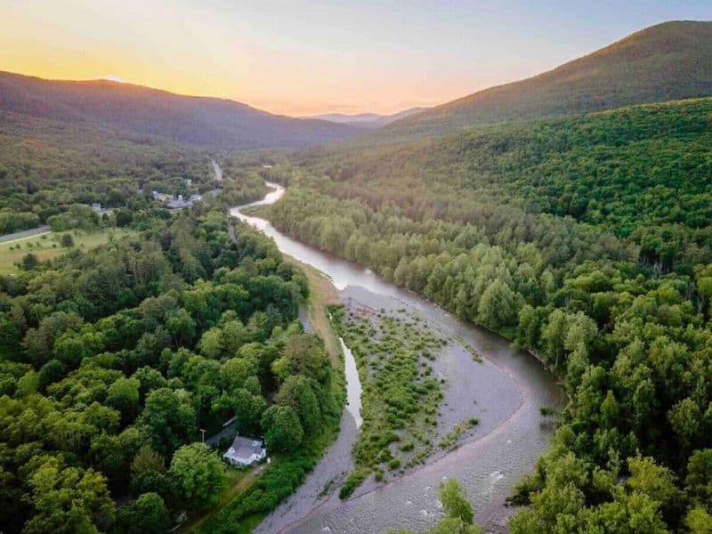 Aerial view of a secluded cozy cabin in the Catskills nestled in a dense forest, beside a winding river.