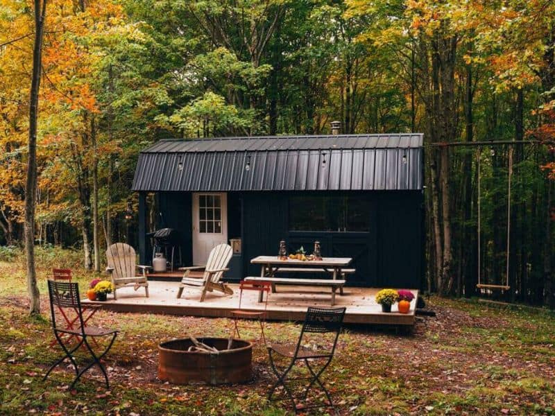 Outdoor setting of a cozy Catskills camping cabin rental featuring Adirondack chairs and a picnic table surrounded by Fall trees.