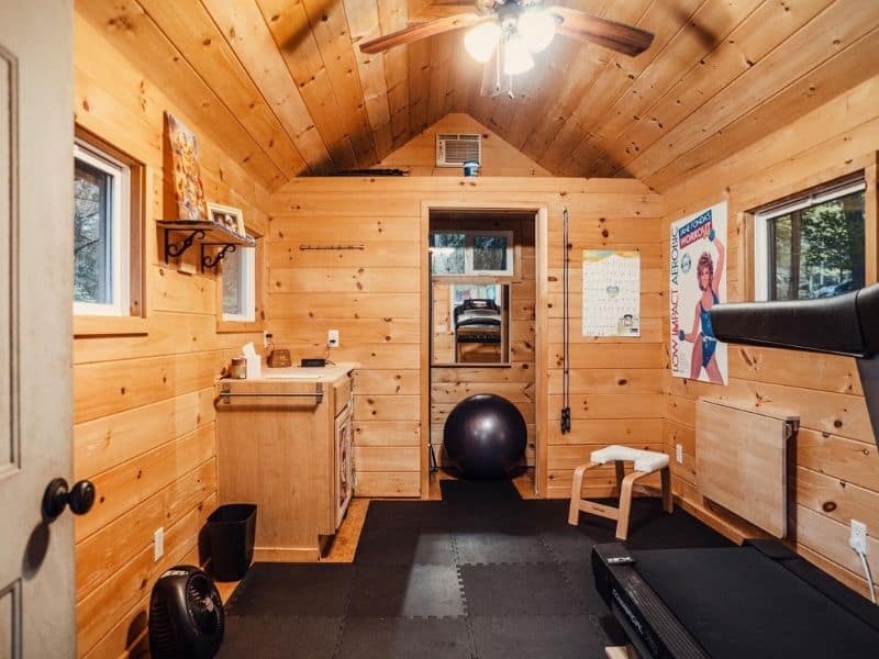 Compact and rustic home gym setup inside a Catskills Vrbo rental, with wooden walls, exercise equipment, and decorative posters.
