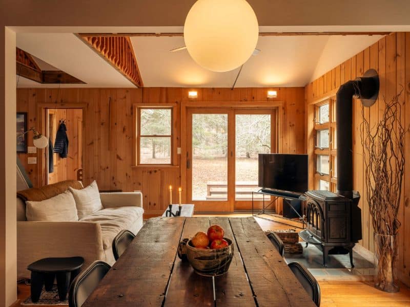 Inviting living and dining area in a Catskills rental, with a rustic wooden dining table, large comfortable couch, and a classic wood stove.