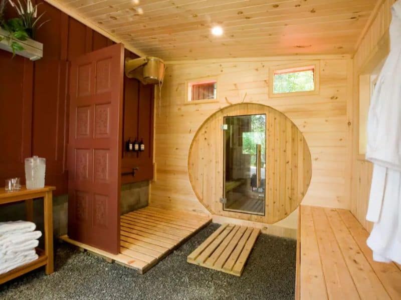 Custom wood built-in sauna in a winter Catskills cabin rental with a round sauna door and a rustic stone floor.